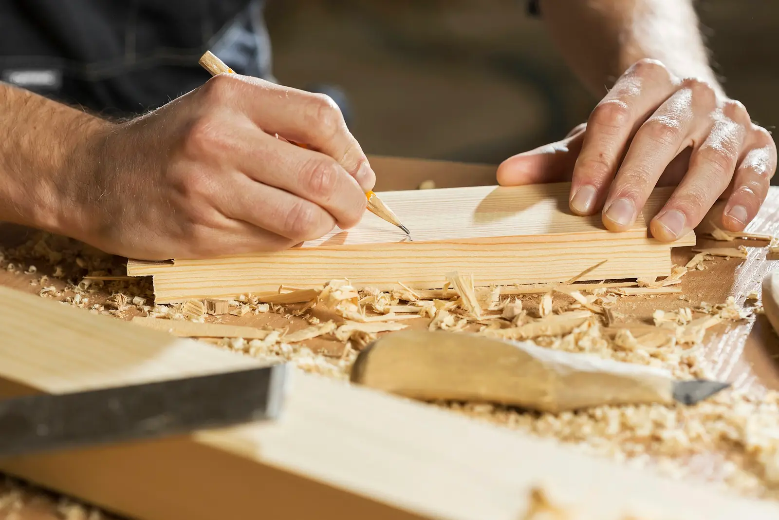 Hände zeichnen mit Bleistift auf einem Holzbrett an, Hobelspäne auf der Werkbank