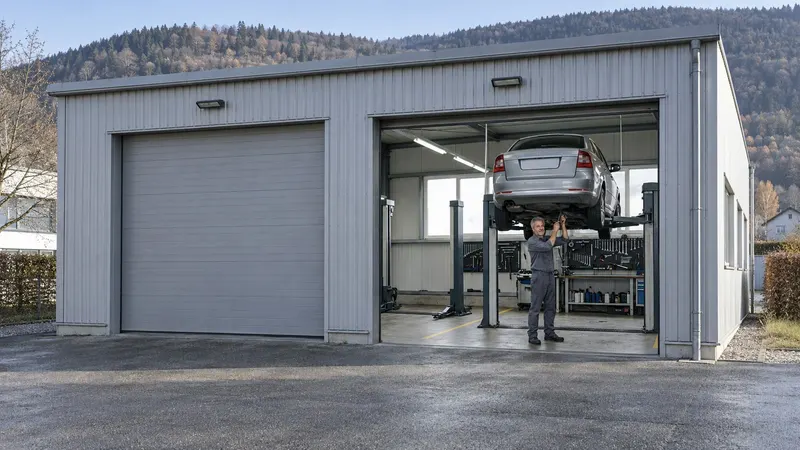 Die Werkstatt der Garage Moser von aussen, im offenen Rolltor arbeitet Marco an einem Auto auf der Hebebühne